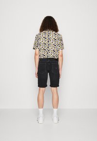 Shorts de mezclilla negros con dobladillos doblados, combinados con una camisa negra de manga corta que tiene un patrón floral blanco y amarillo. Zapatillas blancas.