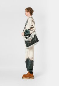 Conjunto crema texturizado con estampados de paisajes, combinado con botas naranjas. Bolso de perfil fino con correa de cadena y diseño único.