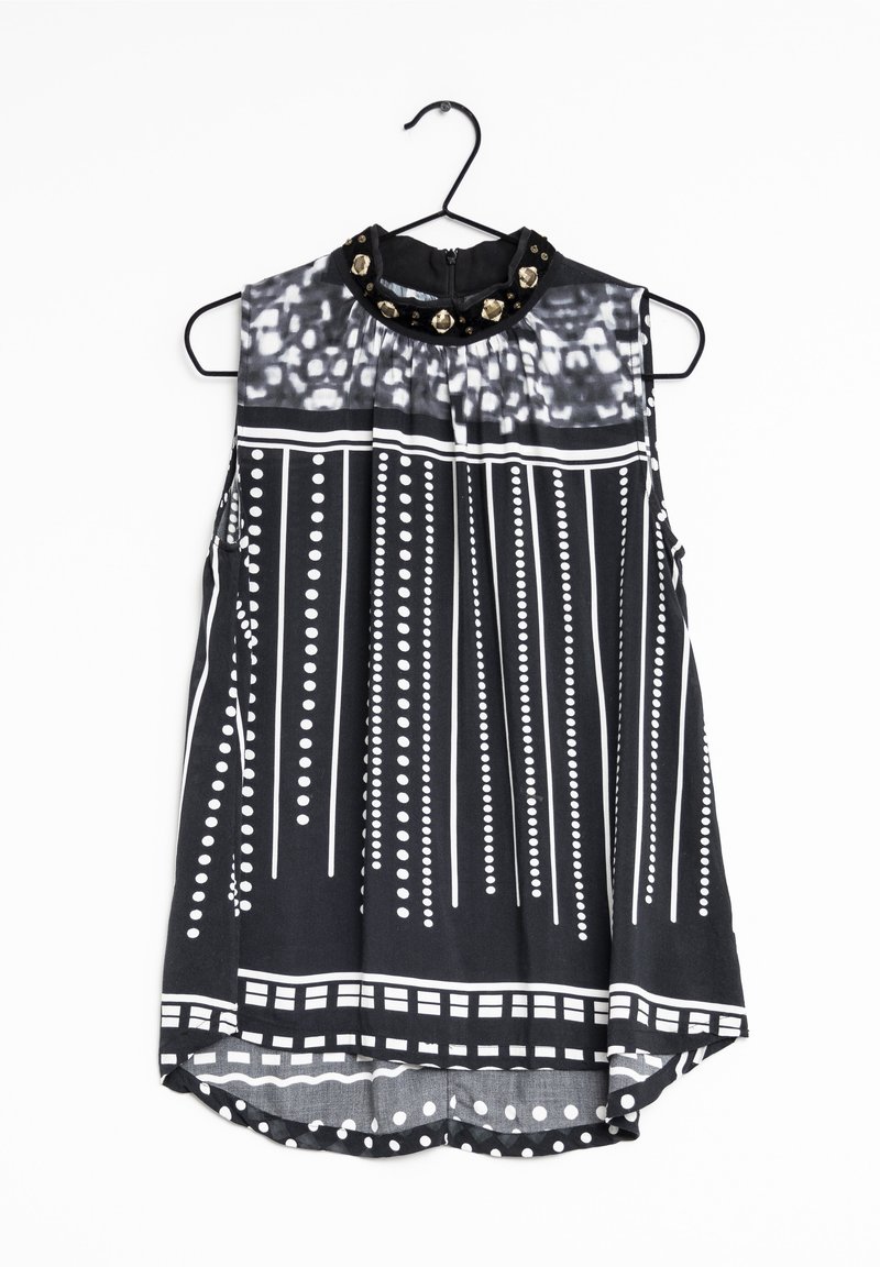 Blusa sin mangas en blanco y negro con un cuello alto, que presenta un diseño plisado, patrones circulares y tachuelas decorativas en el escote.