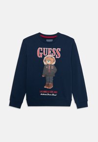 Felpa navy con grafica di un orso in abbigliamento invernale, con lettering rosso "GUESS" e testo sottostante. Collo rotondo e polsini a costine.
