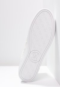 Zapatilla blanca con parte superior texturizada, suela de goma y logo circular en el talón. Acabado liso y diseño plano.