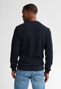 Struktureret navy sweatshirt med rund hals og ribbede manchetter. Båret med lyseblå jeans, som viser diskret accentstikning på lommerne.
