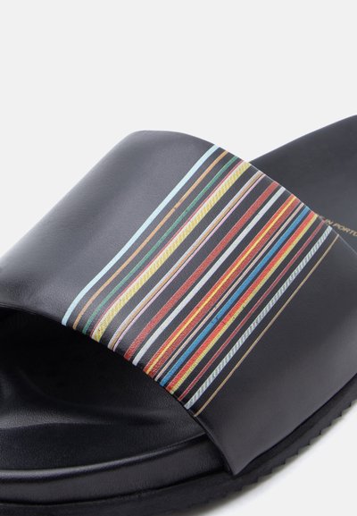 Μαύρο σανδάλι με φαρδιά φάσα που διαθέτει πολύχρωμες κάθετες ρίγες σε κόκκινο, κίτρινο, μπλε, πράσινο και λευκό.
