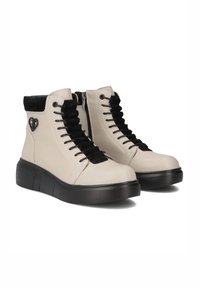 Beżowe buty za kostkę z czarnymi sznurówkami i welurowym kołnierzem, z czarną teksturowaną podeszwą i logo w kształcie serca po boku.