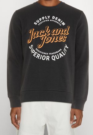 Sweat-shirt noir à manches longues avec logo « Jack and Jones » en orange, entouré de texte blanc « Supply Denim », « Certified Authentic » et « Superior Quality ».