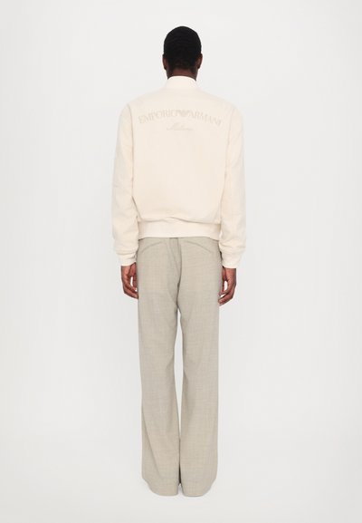 Sweatshirt crème avec logo brodé dans le dos, associé à un pantalon gris clair ample. Texture plate et design décontracté.