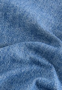 Tessuto di jeans blu con una trama liscia, caratterizzato da un leggero motivo sbiadito. Il materiale sembra resistente e leggermente elasticizzato.