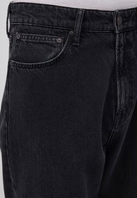 Schwarze Jeans aus Denim verfügen über ein klassisches Fünf-Taschen-Design mit Metallnieten, einem Knopfverschluss und einer leicht abgenutzten Textur.