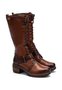 Bottines en cuir marron, à lacets, avec fermeture éclair sur le côté, sangle décorative avec boucle et talon empilé sur fond blanc.