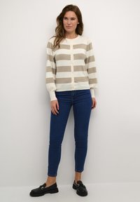 Cream and taupe striped cardigan with a button-down front, long sleeves, and ribbed cuffs, paired with dark blue skinny jeans and black loafers.