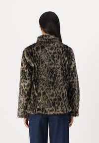 Veste en fausse fourrure imprimé léopard avec une texture douce et un col cranté, comportant de longues manches et une coupe ample, associée à un pantalon en denim foncé.