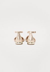 Ballerines métalliques dorées avec un avant tressé, une bride à la cheville et un petit talon rehaussé d'or, conçues pour le confort et un style décontracté.