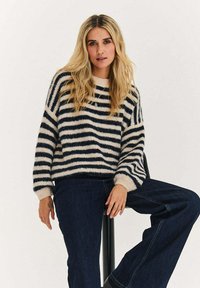 Dzianinowy sweter w granatowo-kremowe paski, z długimi rękawami i okrągłym dekoltem. Połączony z ciemnoniebieskimi szerokimi spodniami jeansowymi.