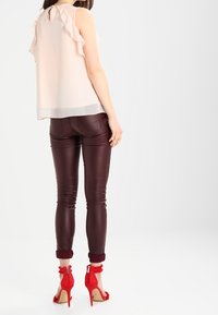 Světle růžová blůza s volánkovým detailem, spárovaná s bordovými úzkými kalhotami a červenými sandály na vysokém podpatku s nártovými pásky a volánkovými akcenty.