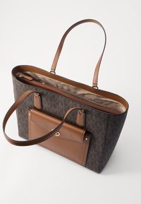 Sac cabas marron avec un motif en monogramme, des accents en cuir, et un grand compartiment ouvert avec une petite poche zippée à l'intérieur.