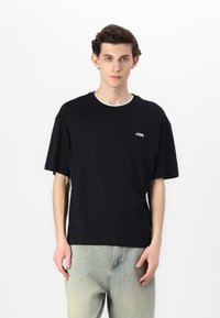 Tricou negru cu mânecă scurtă, fabricat din bumbac, cu un guler rotund cu margine albă și un mic logo alb pe pieptul stâng.