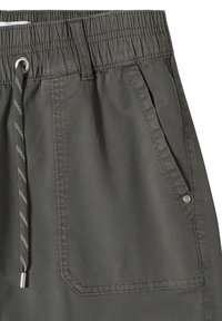 Gros plan sur un pantalon gris foncé à taille élastique avec cordon et une poche plaquée avant avec un rivet métallique sur fond blanc.
