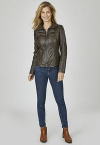 Braune Lederjacke mit einem Reißverschluss vorne, tailliertem Design und großem Kragen. Kombiniert mit dunkelblauen Jeans und braunen Stiefeletten.