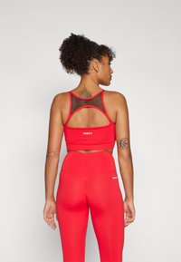 Sujetador deportivo rojo con espalda de malla y logo, combinado con mallas rojas de cintura alta. Textura de tela suave, diseño ajustado, detalles de costura acentuada.