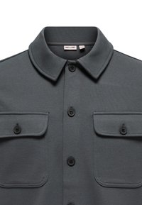 Dunkelgraues Hemd mit Knopfleiste, Kragen und zwei knopflosen Brusttaschen, aus strukturiertem Stoff gefertigt.