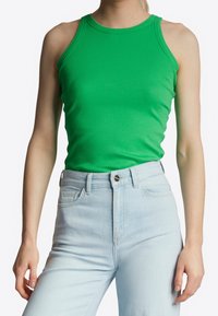 Grøn, ribbet tanktop med rund hals, suppleret af lyseblå højtaljede jeans. Stoffet fremstår glat med en tætsiddende design.