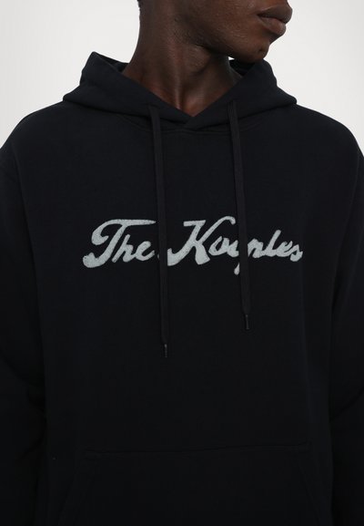 Czarna bluza z kapturem z pastelowym logo "The Kyeples". Wykonana z miękkiego materiału, z kieszenią kangurzą i regulowanym kapturem.