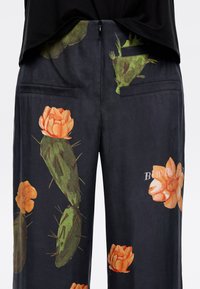 Dark fabric trousers featuring a floral print of orange flowers and green cacti, with two back pockets and a side zipper closure.