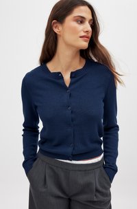 Marineblauwe cardigan met een ronde hals, geribbelde zoom en knoopsluiting. Heeft lange mouwen en een gladde, rekbare brei textuur.