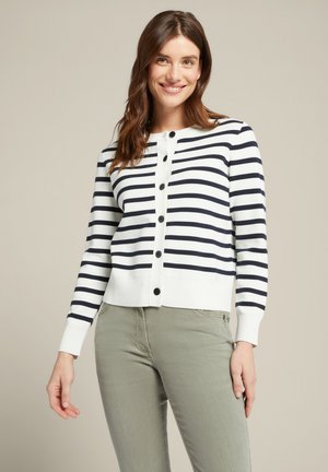 Marineblau- und weiße gestreifte Strickjacke mit langen Ärmeln, rundem Ausschnitt, Knopfverschluss sowie gerippten Bündchen und Saum. Kombiniert mit hellgrünen Hosen.