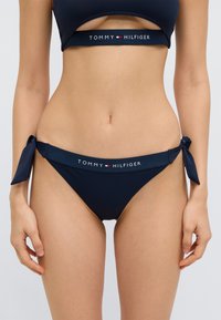 Σετ μπικίνι σε σκούρο μπλε χρώμα με τοπ μπαντόνε με λεπτομέρεια κοψίματος και εσώρουχα με δεσίματα στα πλάγια, κατασκευασμένο από ομαλό, ελαστικό ύφασμα.