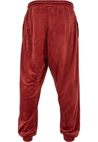 Red, velvety joggers with an elastic waistband, side pockets, and ribbed cuffs at the ankles, featuring a relaxed, tapered design.