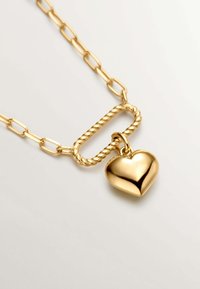 Collar de cadena de oro con eslabones alargados, un centro ovalado retorcido y un colgante en forma de corazón pulido.