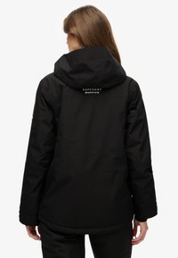 Czarna wodoodporna kurtka z kapturem, z logo "Superdry Mountain", o standardowym kroju i gładkiej, zewnętrznej fakturze.