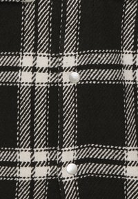 Sort og hvid ternet flannelstoffe med en blød tekstur. Har et markant ternet m�ønster og nikkel-lignende knapper langs placket.