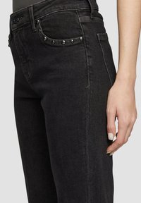Jeans in denim nero con un design aderente, caratterizzati da borchie argentate sulla tasca anteriore e una texture liscia. Stile classico a cinque tasche.