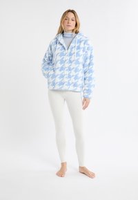Niebiesko-biała bluza polarowa w wzór pepitki, z przednim zamkiem błyskawicznym, ściągaczami i długimi rękawami, zestawiona z białymi legginsami.