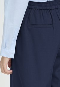 Tumesiniseid pükse puuvillasegust elastse vöökohaga ja tagataskuga, kombineeritud helesinise pikakäise särgiga, millel on nööbitavad varrukakuvad.