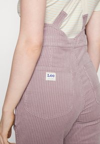 Lee-märkta, ljuslila corduroy-hängselbyxor med vertikala ränder, som har justerbara axelremmar och fickor på baksidan.