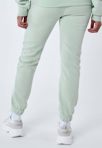 Pantalones de chándal verde claro con puños ajustados, hechos de una tela suave. Combinados con zapatillas blancas con acentos grises y suelas texturizadas.