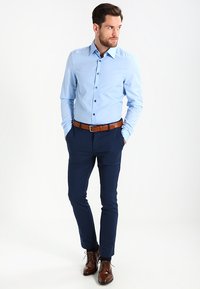 Lyseblå skjorte med knapper, mørk marineblå bukser, brun belte og brune pensko. Skjorten har knapper og en skreddersydd design.