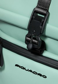 Een mintgroene tas met een zwarte rits en gesp als sluiting. Het ontwerp heeft een getextureerd oppervlak met een strak, modern stijl.