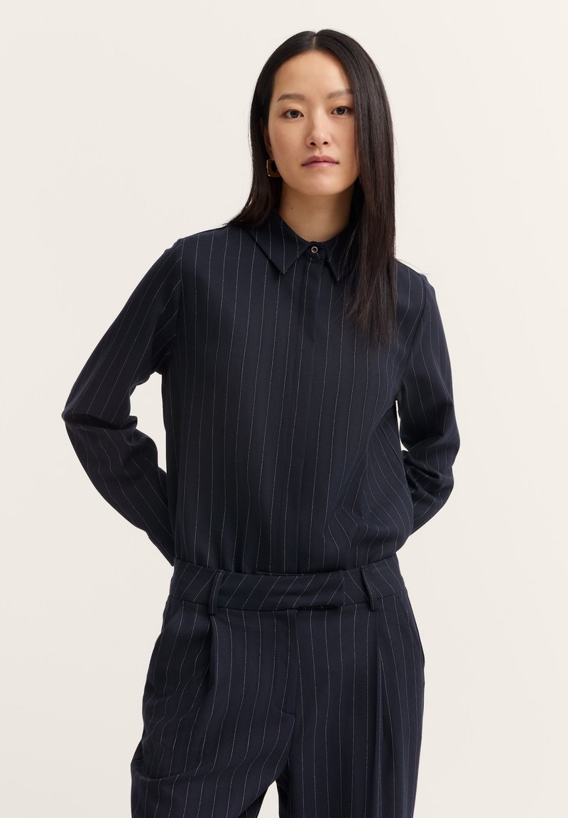 Navy blue pinstriped long-sleeve shirt with a button collar, featuring a straight cut and smooth fabric texture. Combined with tailored pants.