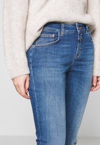 Denim jeans in medium blue with a slim fit, five-pocket design, subtle whiskering, and stitching accents. Cotton material with slight stretch.