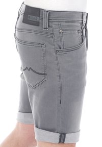 Graue Jeansshorts mit umgeschlagenem Saum, ausgestattet mit einem schwarzen Label mit der Aufschrift "MUSTANG True Denim" und dekorativen Nähten auf den Gesäßtaschen.