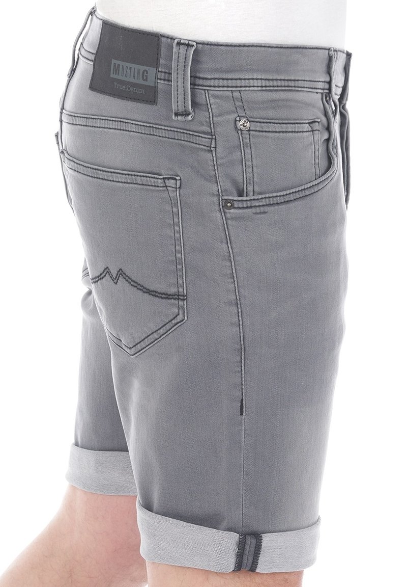 Graue Jeansshorts mit umgeschlagenem Saum, ausgestattet mit einem schwarzen Label mit der Aufschrift "MUSTANG True Denim" und dekorativen Nähten auf den Gesäßtaschen.