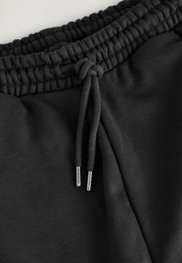 Black sweatshirt fabric featuring an elastic waistband with a drawstring, showcasing textured surface and metal tip accents.