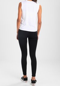 Leggings elásticos negros de tela suave, combinados con una camiseta sin mangas blanca. Presenta costuras laterales y bolsillos en la parte posterior.
