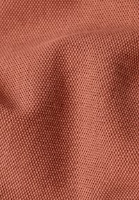 Tessuto testurizzato in un colore terracotta tenue, con un motivo intrecciato e una superficie morbida e leggermente elastica.