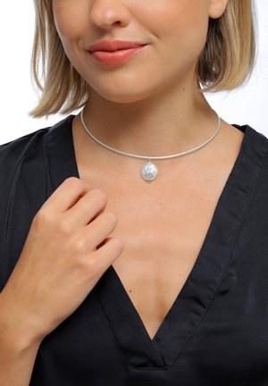 Silberner Halsreif mit einem runden, strukturierten Anhänger. Das Halsband ist elegant, mit einer glatten Oberfläche und dezentem Glanz. Schwarzes Oberteil sichtbar.