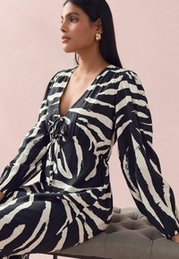 Robe à imprimé zèbre noir et blanc avec manches longues, décolleté plongeant et détail à nouer à la taille, fabriquée dans un tissu léger.